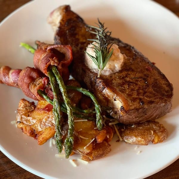 Grilled steak with a dollop of butter and rosemary, bacon-wrapped asparagus, and smashed potatoes.