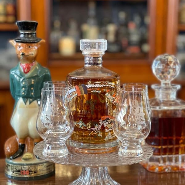 A decorative bottle of Hibiki Japanese Harmony whiskey with two glasses on a stand.