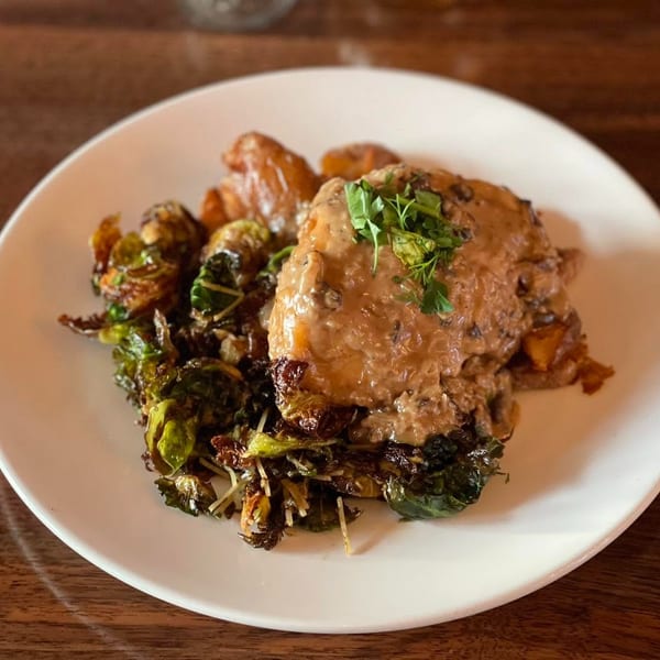Chicken with mushroom gravy, roasted potatoes, and crispy Brussels sprouts on a white plate.