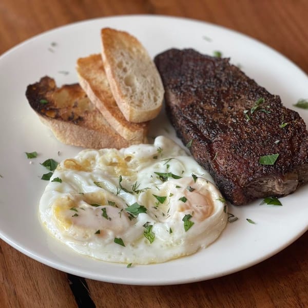 Steak and eggs breakfast with toasted baguette slices on a white plate.